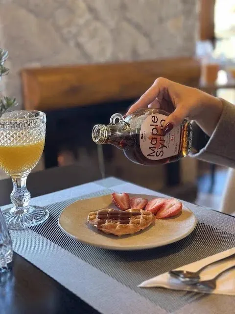 Maple syrup sendo servido sobre waffle com morangos junto à lareira da Pousada Maple