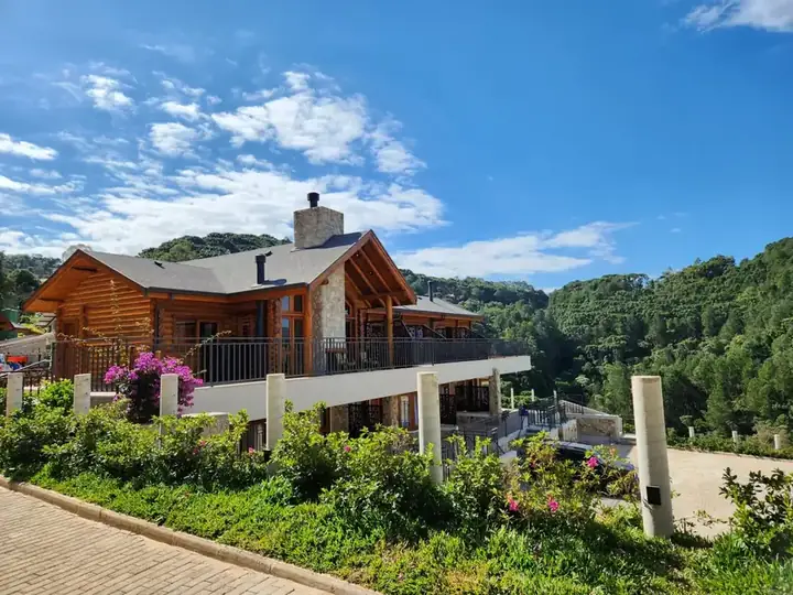 Fachada da Pousada Maple Monte Verde em dia de sol, cercada pela mata da Serra da Mantiqueira